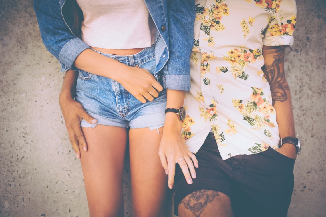 Cropped midsection of a hipster couple standing close together and leaning against a wall in retro style clothing