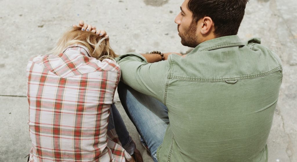 Smutná žena sedí vedľa partnera s hlavou v rukách