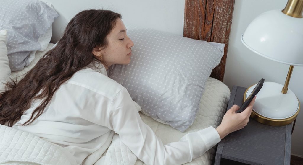 Žena v posteli pozerá do mobilu